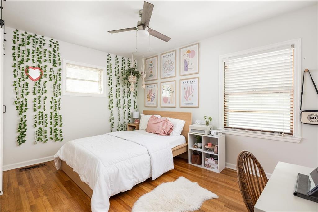 Bedroom with white bedding, pink pillows, trailing wall vines, framed art, and hardwood floors.