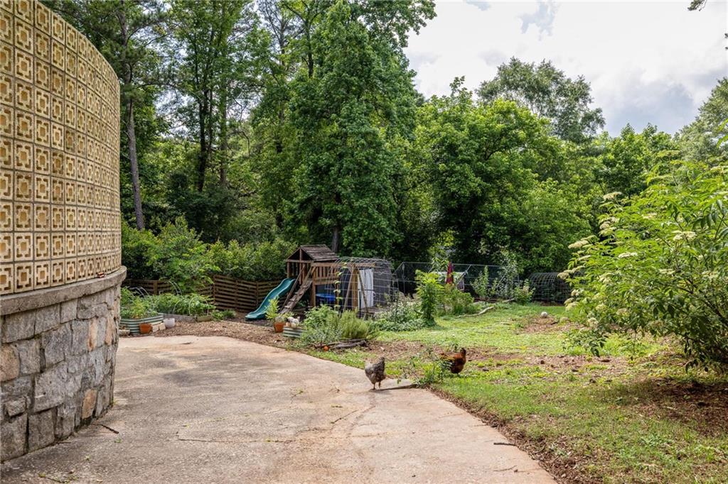 Backyard patio beside a patterned masonry wall, with chickens, garden beds, and a children's playset.