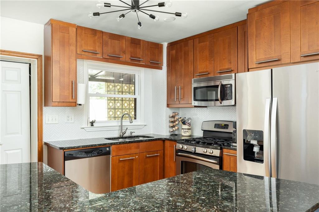 Kitchen with warm wood cabinets, dark stone counters, stainless steel appliances, and a window above the sink.