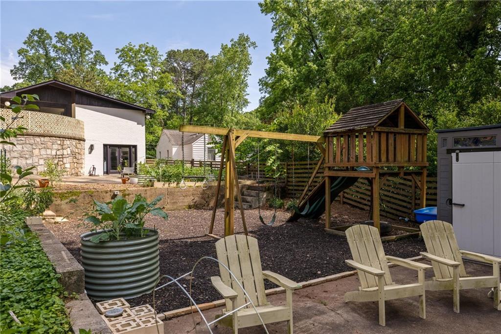 Backyard with a wooden playset, swings, patio chairs, and raised garden bed.