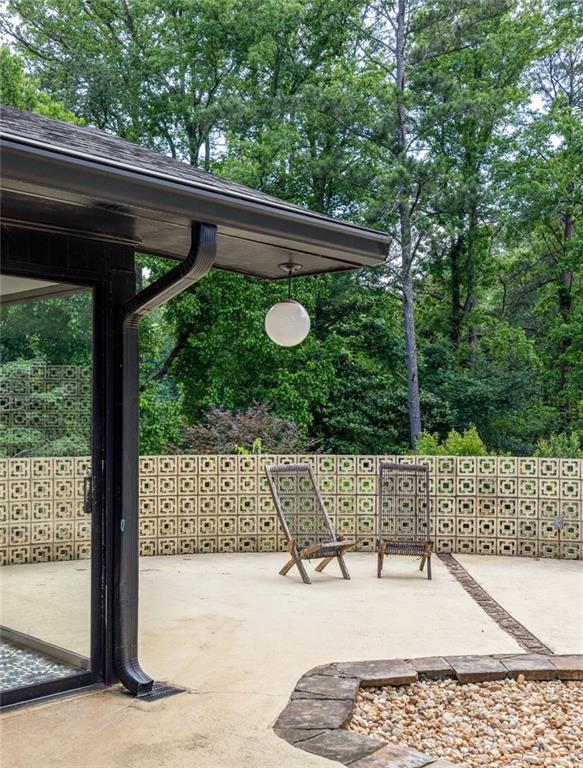 Patio with woven chairs, patterned breeze-block wall, and wooded backdrop.