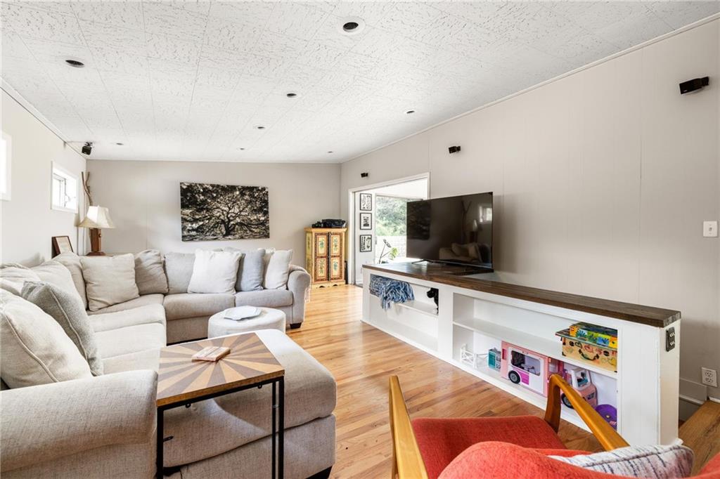 Living room with a pale sectional, television, wood floors, and colorful accent chairs.