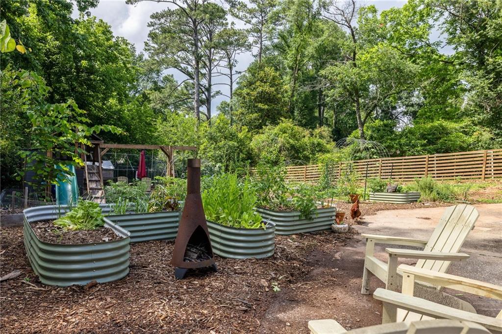Backyard garden with raised beds, a metal chiminea, Adirondack chairs, and a wooden fence.