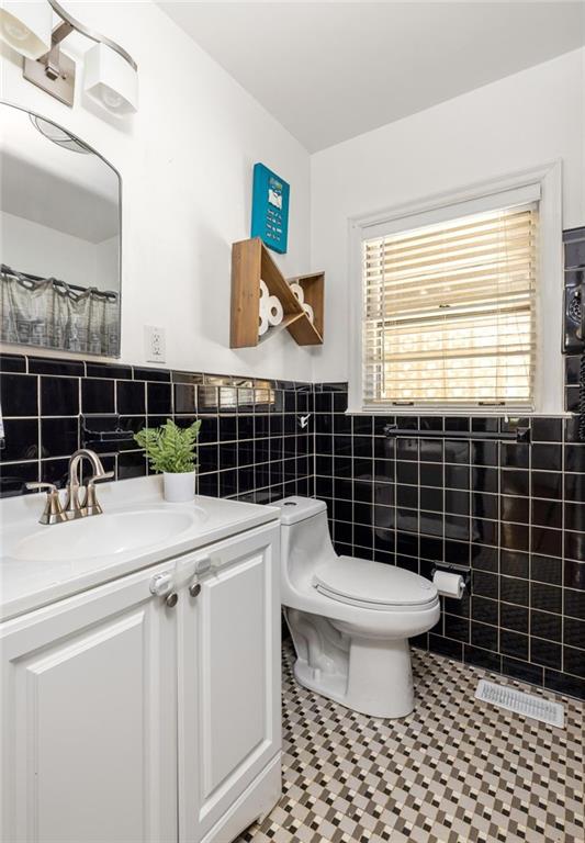 Bathroom with black tile, white vanity and toilet, and a geometric mosaic floor.