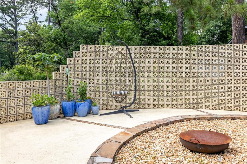Patio with a hanging egg chair, blue planters, patterned privacy wall, and gravel fire pit.