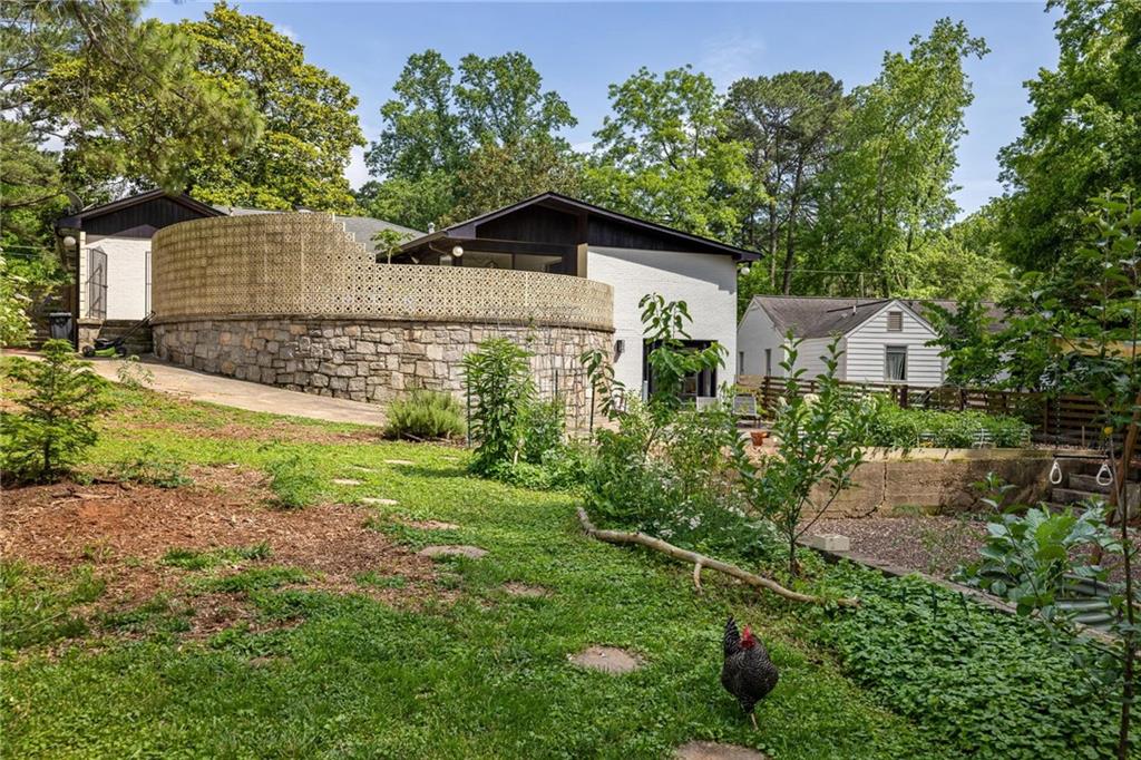 Modern home behind a stone retaining wall and patterned screen, with a landscaped yard and chicken.