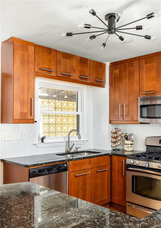 Kitchen with warm wood cabinetry, dark stone counters, stainless steel appliances, and a window above the sink.