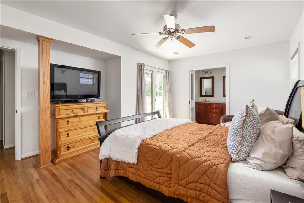 Furnished bedroom with a rust-colored quilt, hardwood floors, and an open doorway to the bathroom.