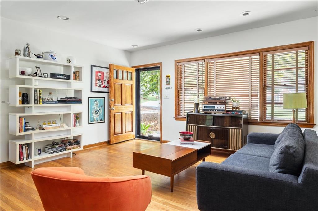Living room with hardwood floors, built-in bookshelves, large wood-blind windows, and a vintage stereo console.