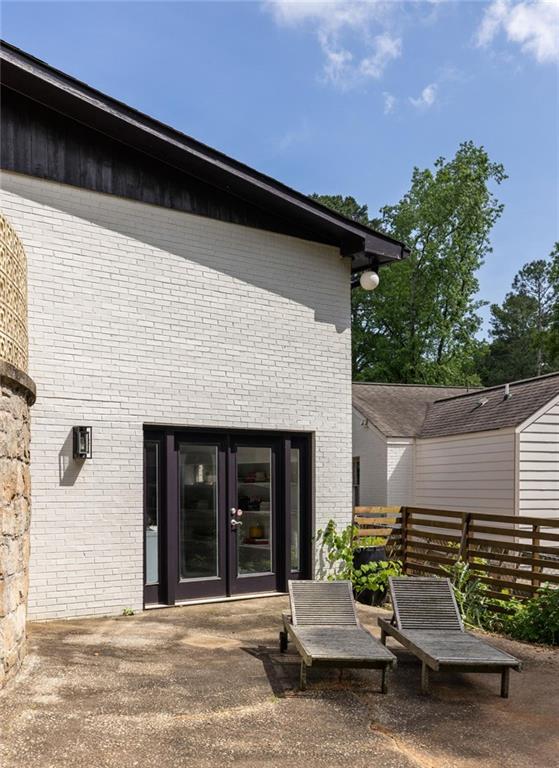 Rear patio with white brick exterior, dark-framed glass doors, lounge chairs, and a wood privacy fence.