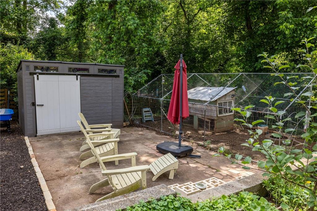 Backyard patio with Adirondack chairs, a red umbrella, storage shed, and fenced chicken coop.