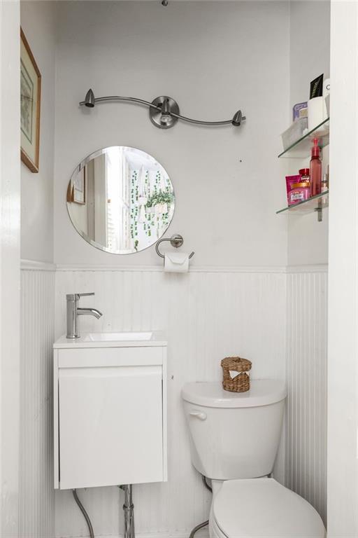 Bright white bathroom with beadboard walls, an oval mirror, and glass shelves beside the toilet.