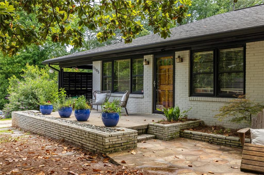 White-brick home with a raised stone patio, blue planters, and a wood front door.