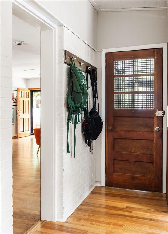 Entryway with a gridded-glass wood front door, white brick walls, and hardwood floors.