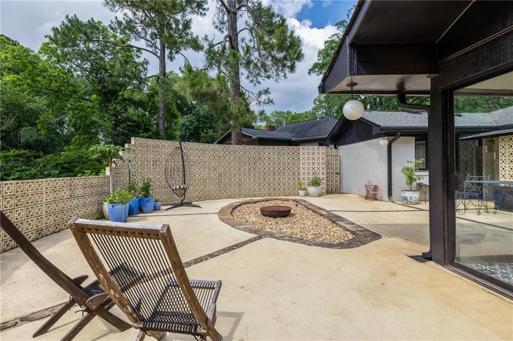 Concrete backyard patio with a central fire pit, patterned privacy wall, and outdoor seating.