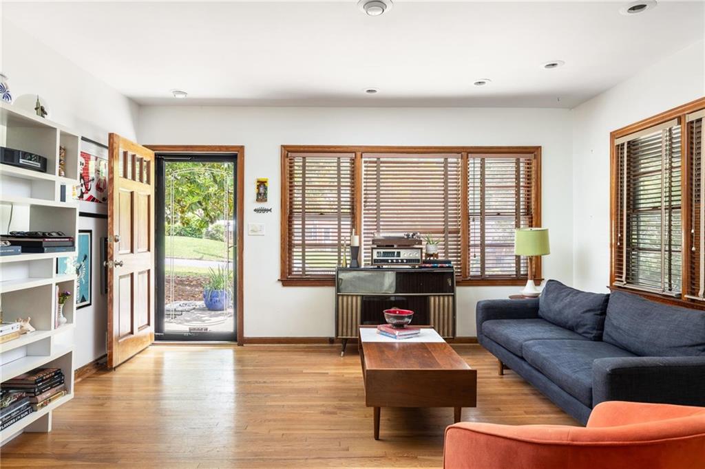 Living room with hardwood floors, blue sofa, orange chair, and open door to the garden.