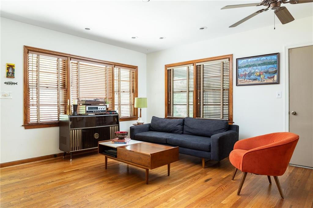 Living room with hardwood floors, wood-blind windows, a dark sofa, and an orange accent chair.