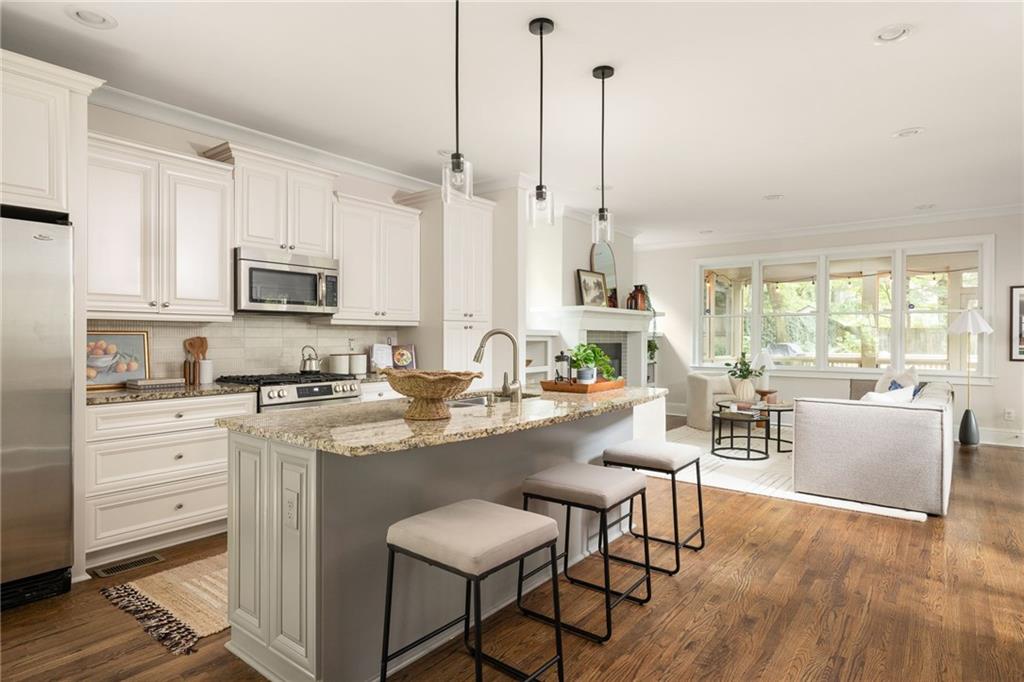 Bright kitchen with a large stone island and bar stools opening into a living area.