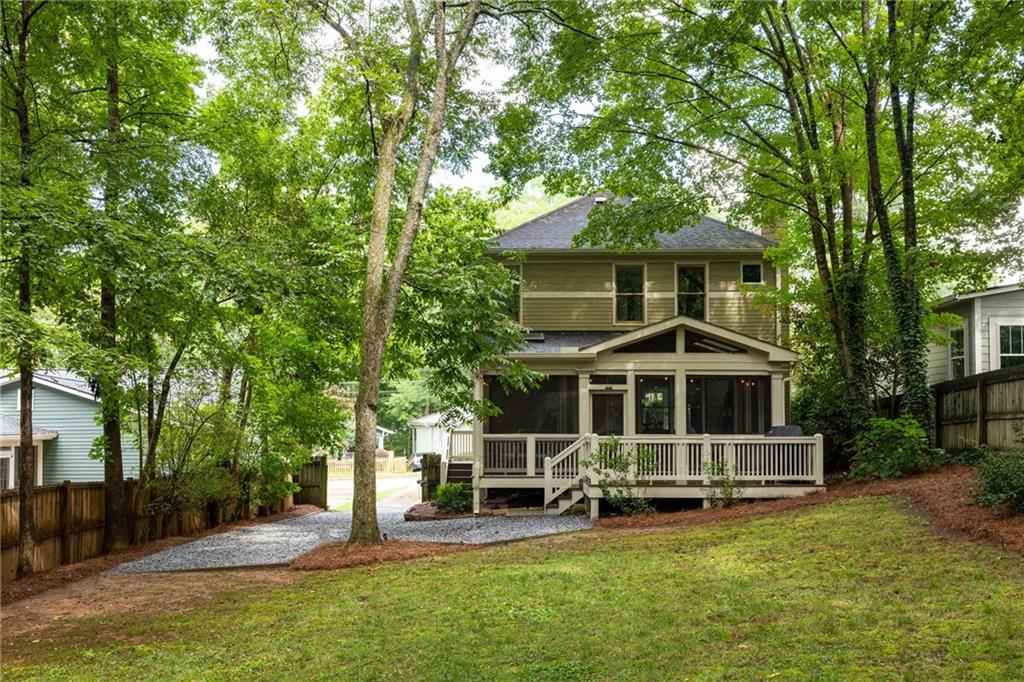 Two-story home with a raised covered porch, gravel path, and mature trees surrounding the yard.