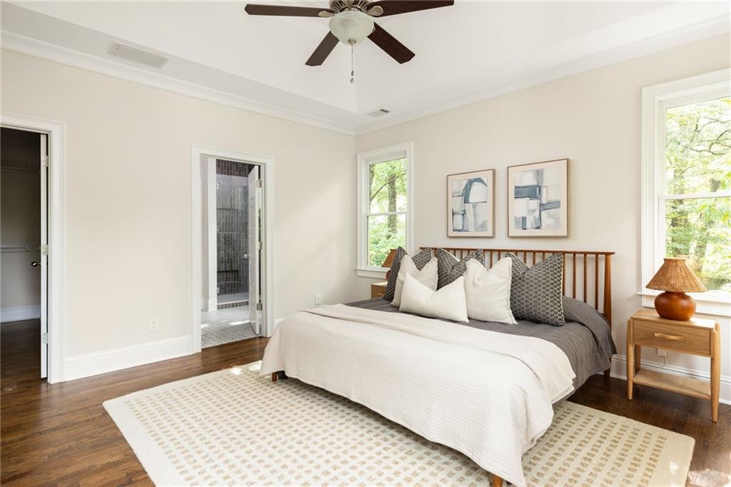 Bedroom with a wood-frame bed, white bedding, hardwood floors, and windows overlooking trees.