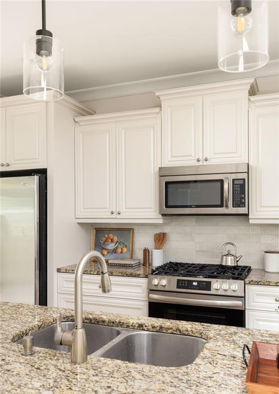 Kitchen with white cabinets, granite island, double sink, and stainless-steel appliances.