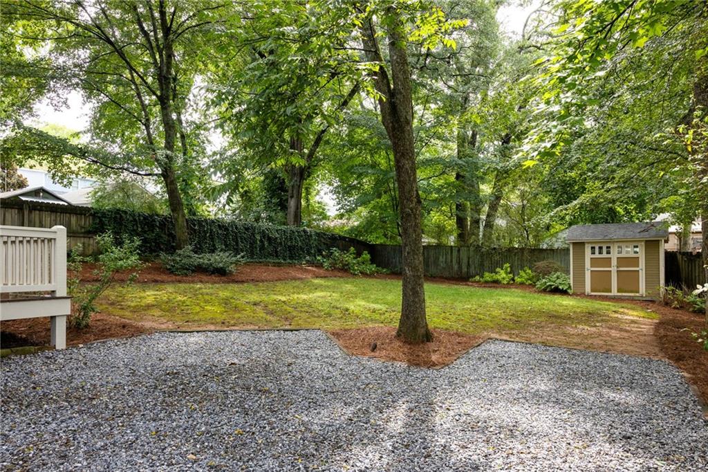 Shaded backyard with mature trees, a gravel parking area, lawn, and a small shed.