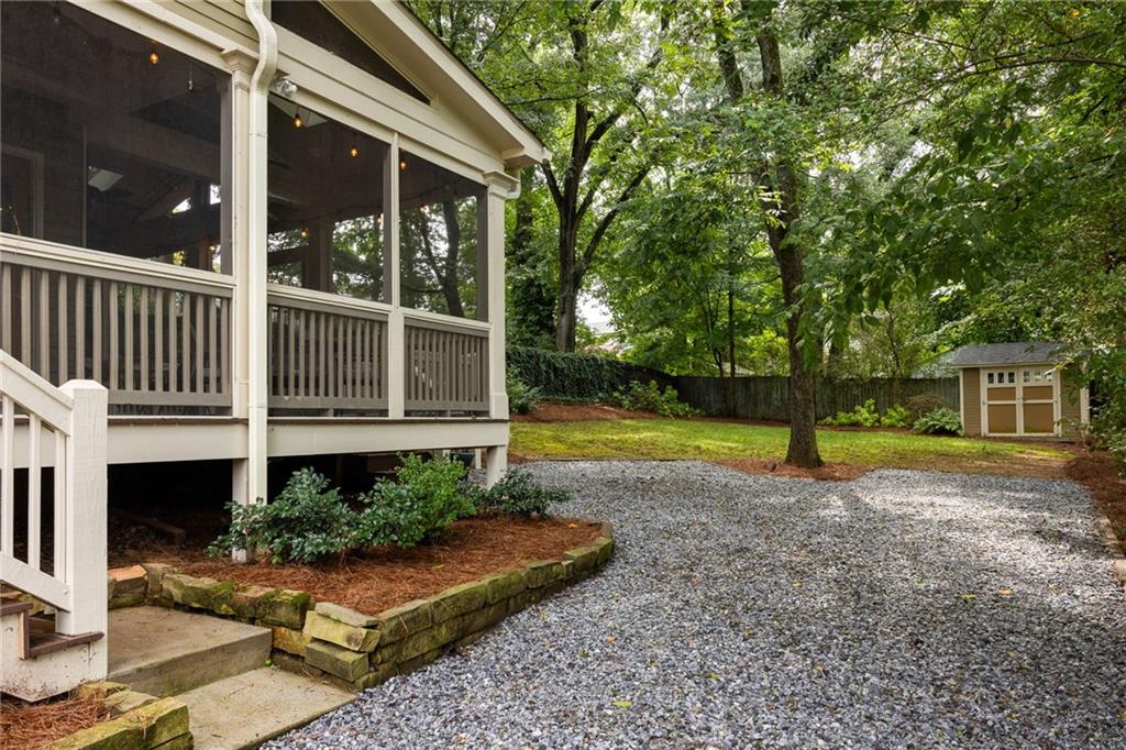 Screened porch beside a gravel driveway, landscaped yard, and small storage shed.