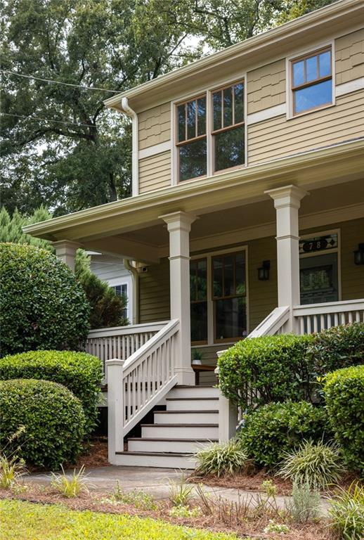 Two-story home entrance with a covered porch, white columns, steps, and trimmed shrubs.
