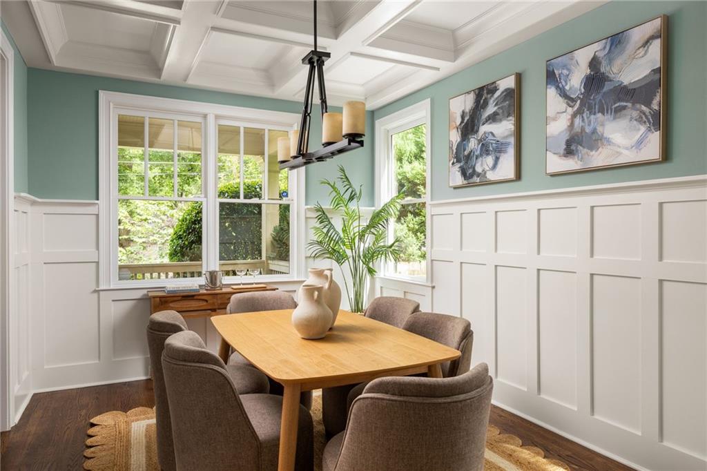 Dining room with a coffered ceiling, white wainscoting, and large windows overlooking greenery.