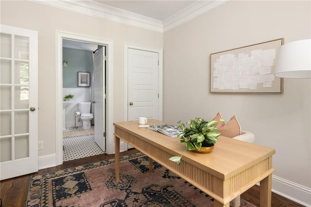 Home office with a long wooden desk and patterned rug beside an open bathroom doorway.