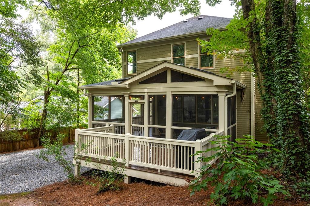 House rear with a screened porch and raised deck surrounded by mature trees.