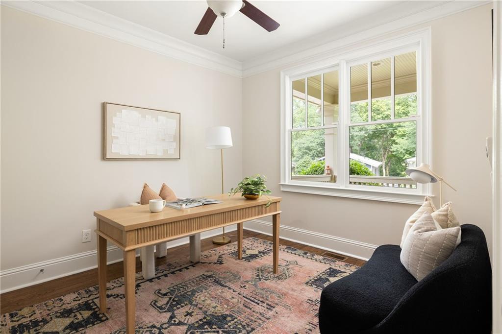 Bright home office with a wooden desk, large windows, and a dark lounge chair.