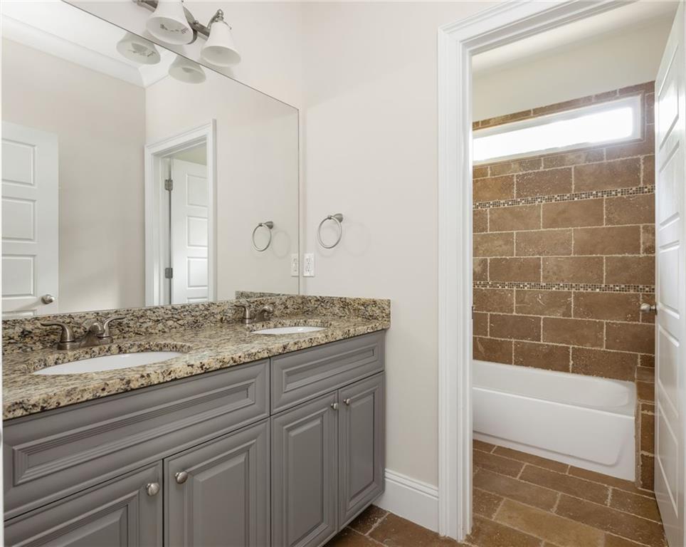 Bathroom with a double-sink gray vanity and granite counter beside a brown-tiled bathtub.