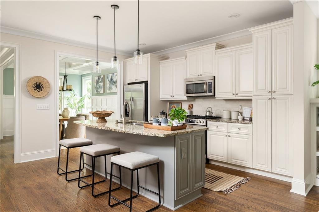 Kitchen with white cabinets, stainless steel appliances, and a gray island with three stools.