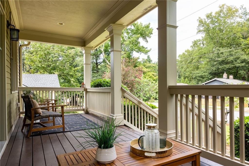 Covered porch with white railings, two chairs, and a low table with a potted plant.