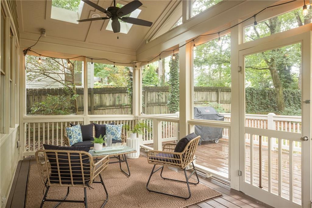 Screened porch with wicker seating and a ceiling fan overlooking a wooden deck and leafy yard.