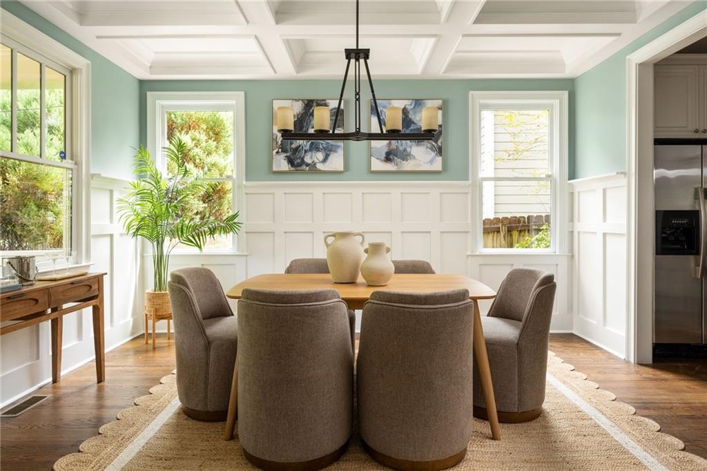 Dining room with a round table, upholstered chairs, sage-green walls, and a coffered ceiling.