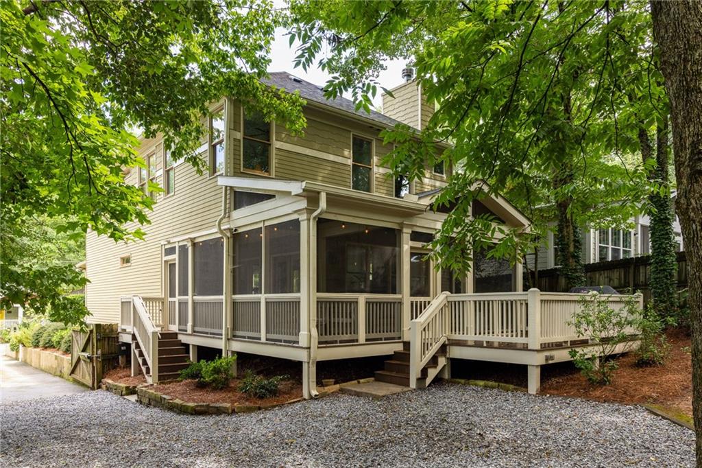 Two-story beige house with a screened porch and raised deck beneath leafy trees.