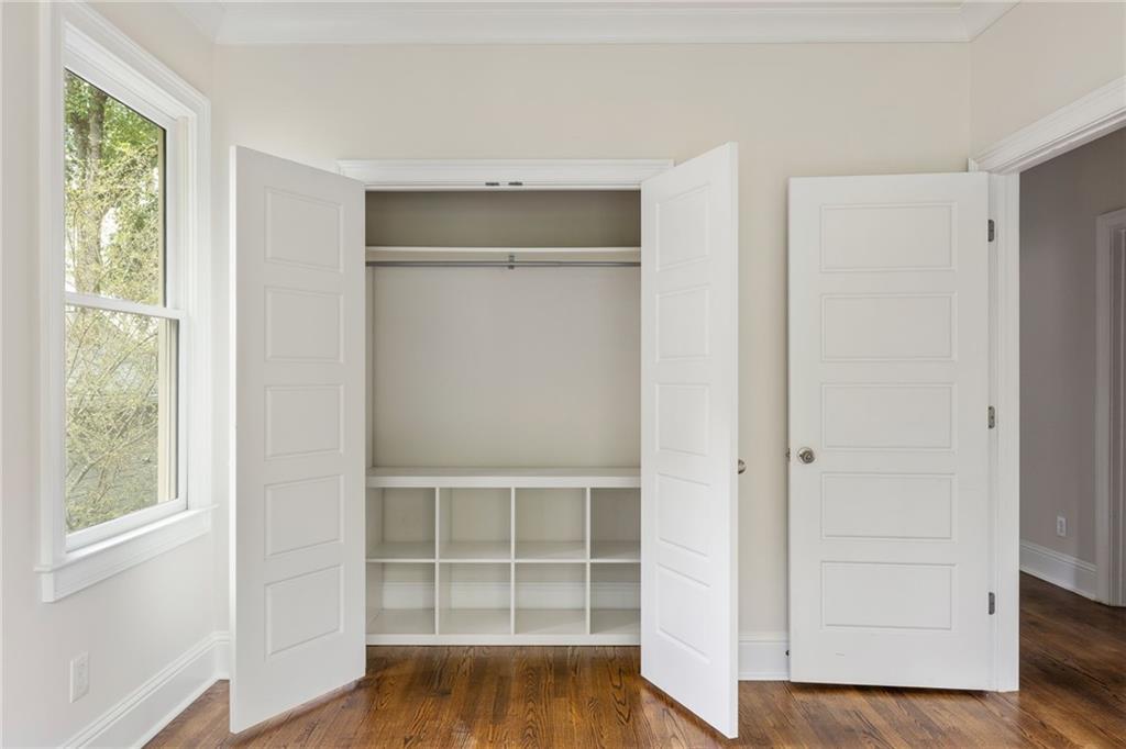 Empty room with an open built-in closet, cubby shelves, a large window, and hardwood floors.
