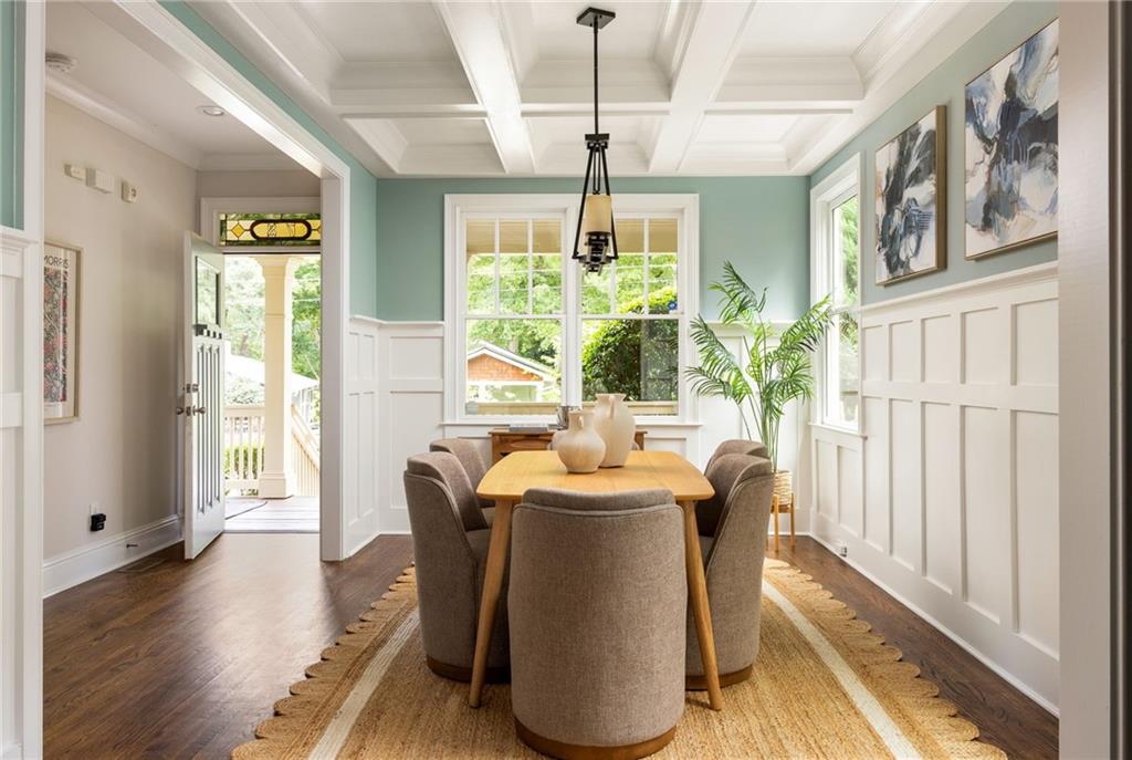 Dining room with a coffered ceiling, white wainscoting, and a table beside an open porch doorway.