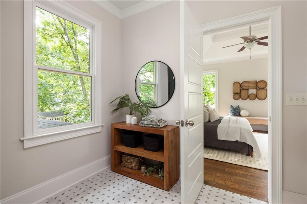 Tiled bathroom area with a round mirror and wooden console, opening into a bedroom.