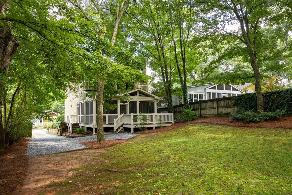 Rear exterior of a light-sided home with a screened porch, deck, and wooded lawn.