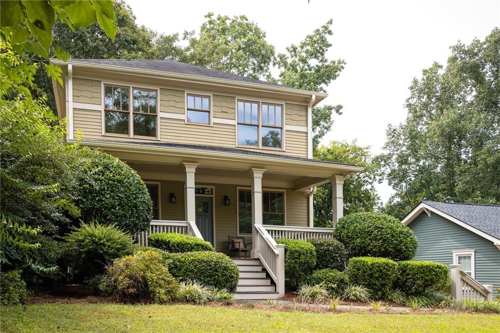 Two-story beige house with a covered porch, white railings, front steps, and mature shrubs.