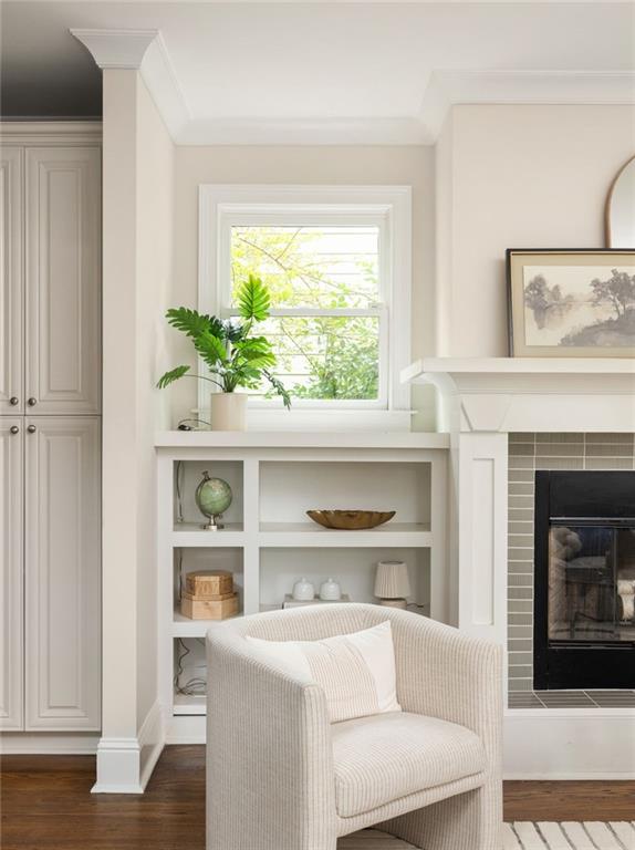 Living room with a white armchair, built-in shelves, and a tiled fireplace beside a bright window.