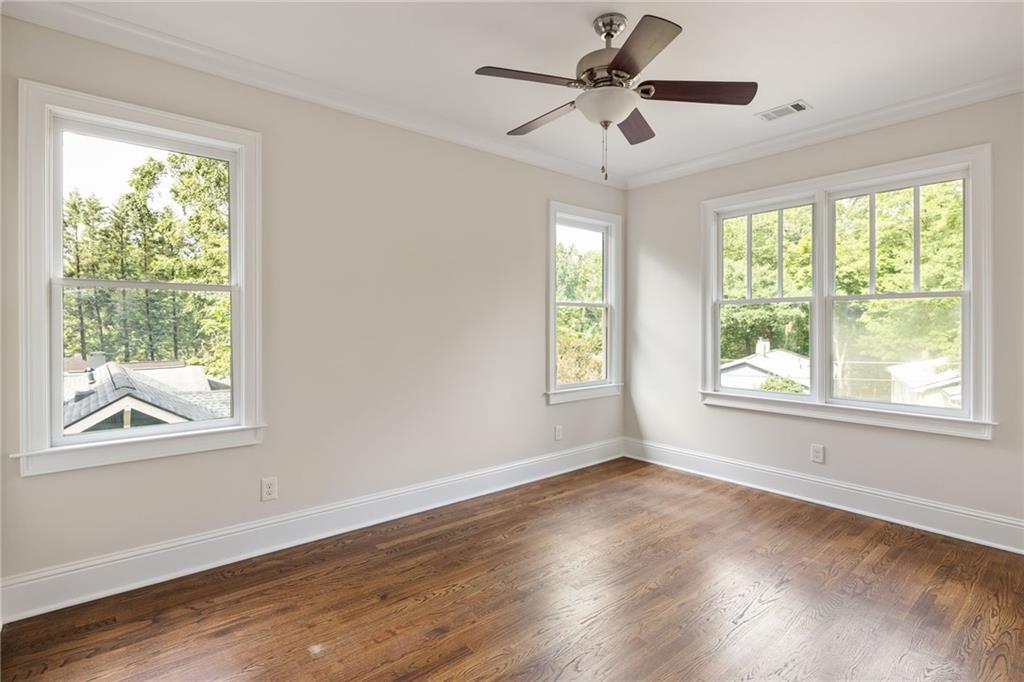 Empty bedroom with hardwood floors, three windows overlooking trees, and a ceiling fan.
