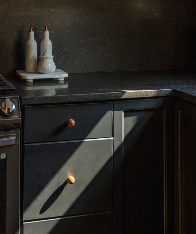 Kitchen corner with charcoal cabinets, dark stone counters, and sunlight across brass drawer pulls.