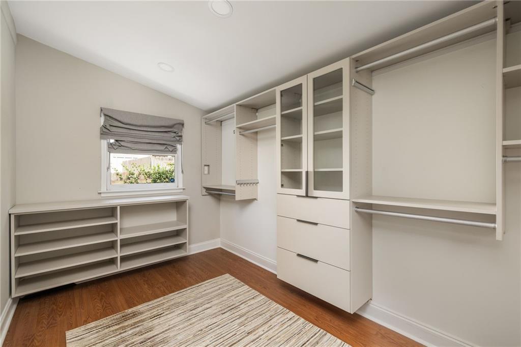 Walk-in closet with white built-in shelving, glass-front cabinets, and hardwood floors.