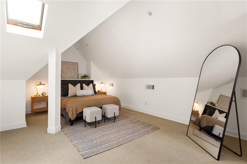 Attic bedroom with a skylight, sloped ceiling, and arched floor mirror.