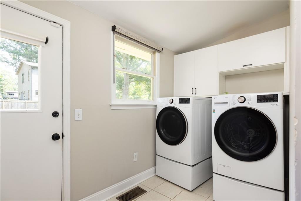 Laundry room with front-loading washer and dryer, white cabinets, and a window.