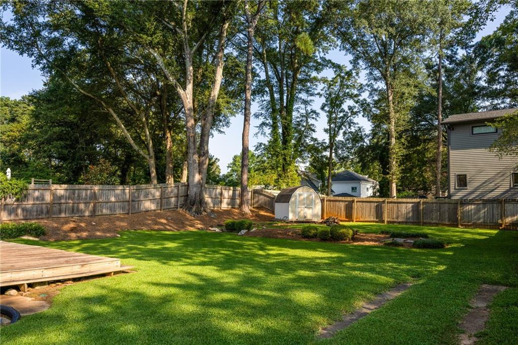 Fenced backyard with a broad lawn, mature trees, a small shed, and part of a wooden deck.